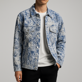 Men’s light blue floral-patterned denim-look trucker jacket with distressed detailing, worn over a white t-shirt and paired with black pants against a neutral background.