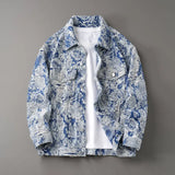 Flat lay of a blue and beige floral-patterned distressed denim-look trucker jacket layered over a white t-shirt on a gray background.