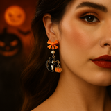 Close-up of a woman wearing Halloween-themed earrings with pumpkins and cats, with pumpkins in the background.