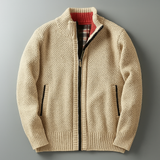 Beige knitted zip-up cardigan laid flat on grey surface, featuring ribbed cuffs, black zip lining, and red inner collar detail - luxury textured knitwear for men.