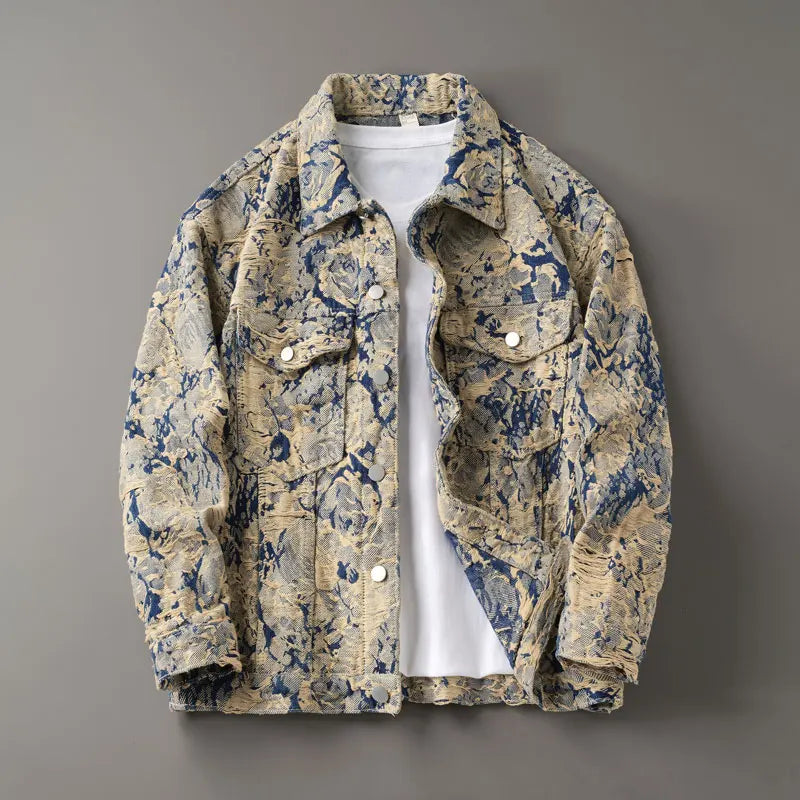 Men’s floral-patterned textured denim-look trucker jacket in beige and navy tones, featuring buttoned chest pockets, long sleeves, and a white shirt layered underneath, displayed flat on a gray background.
